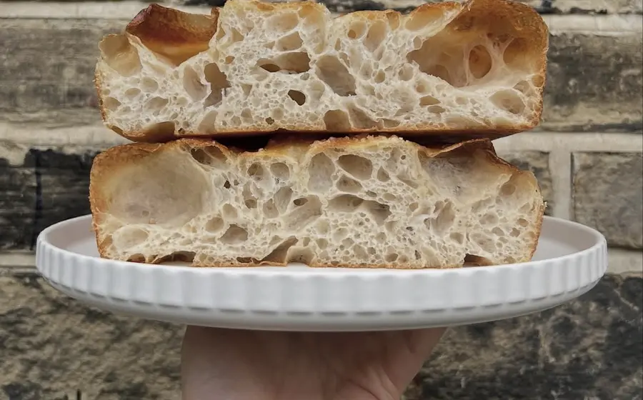focaccia on a plate being held up with a wall in the backdrop