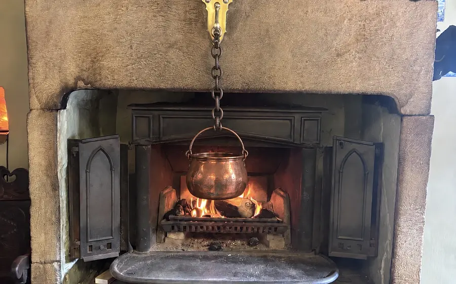 fireplace with brass hook set to one side and copper pan hanging from it