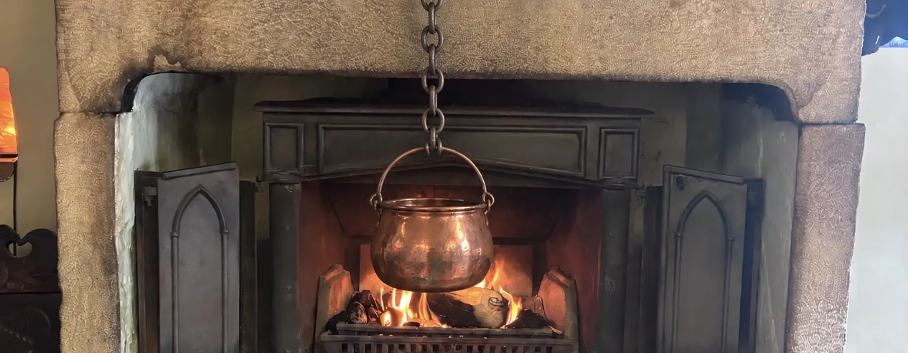 fireplace with brass hook set to one side and copper pan hanging from it